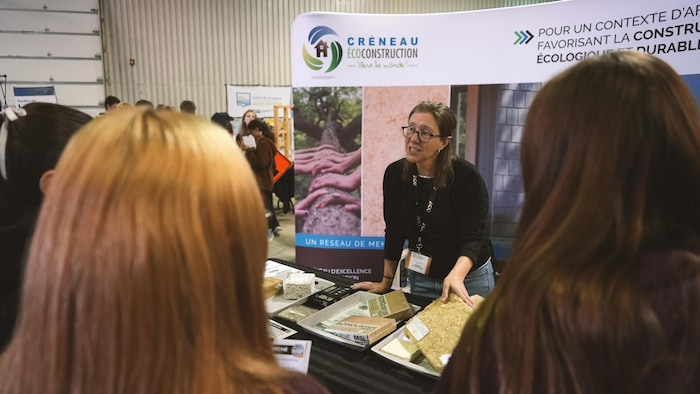 Une exposante dans un salon de la construction s'adresse à des jeunes. 