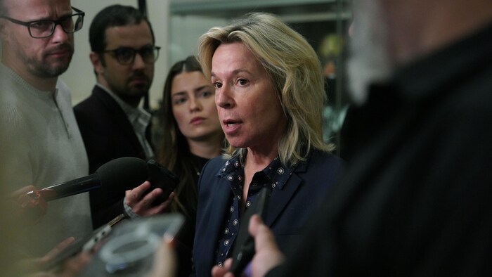 Une personne entourée de journalistes dans une mêlée de presse.