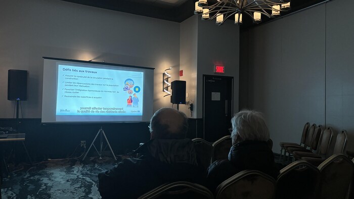 Deux personnes regarde une vidéo projetée sur un mur.