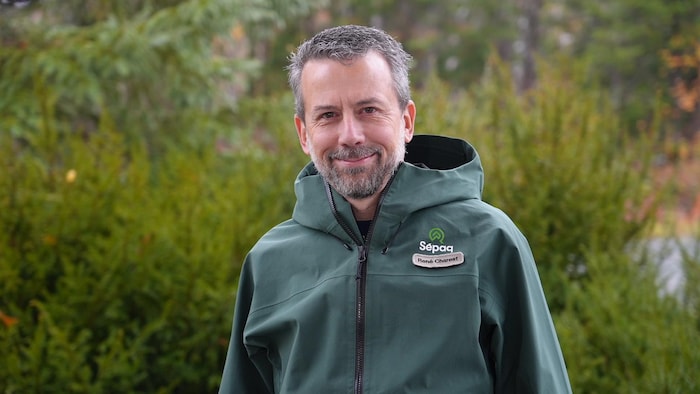 René Charest pose devant la forêt avec un imperméable vert.