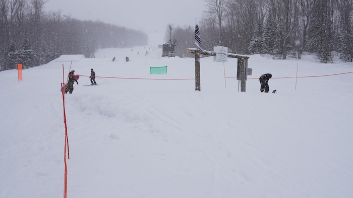Une piste du Mont-Comi sous la neige, avec plusieurs planchistes.