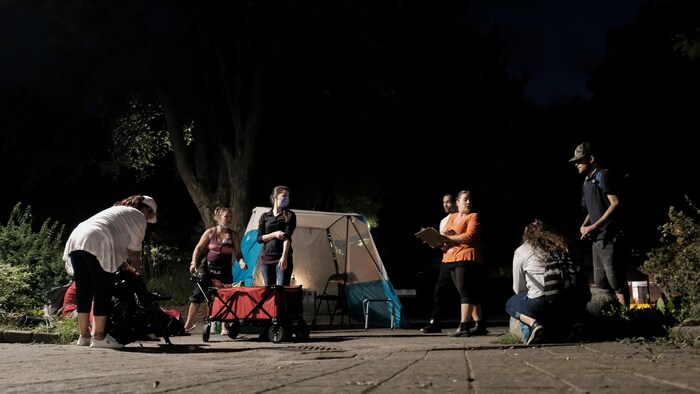 Un campement au centre-ville de Sudbury avec plusieurs personnes qui discutent le soir.