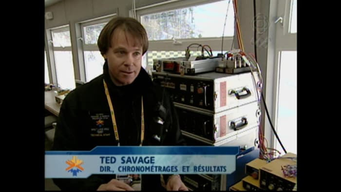 L'homme est devant des installations techniques. Au bas de l'image, sur une bande il est écrit son nom, directeur chronométrages et résultats.