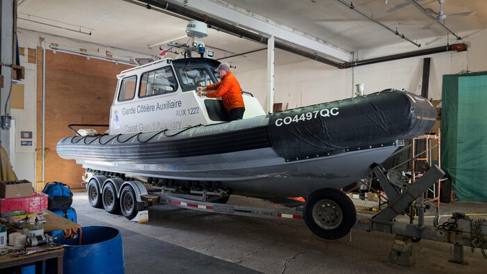 L'homme debout sur un petit bateau qui est rangé dans un garage.
