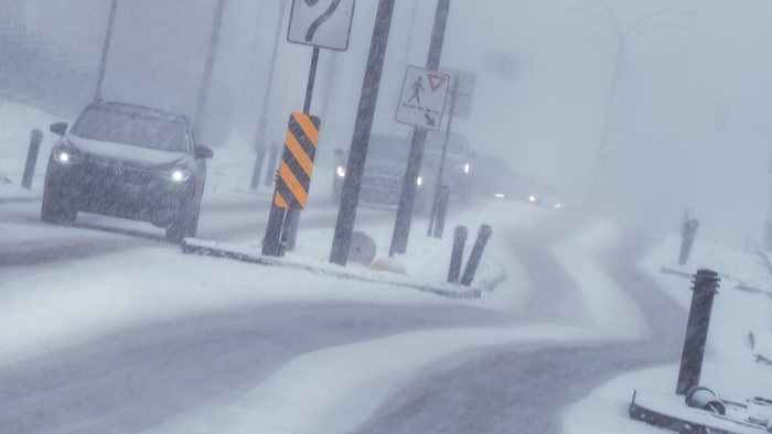 Des voitures circulent sur une route dans des conditions météo difficiles.