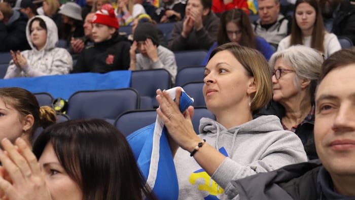 Une femme assise dans un aréna tient un drapeau de l'Ukraine