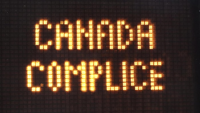 Un panneau numérique de limite de vitesse affiche le message « CANADA COMPLICE ». 