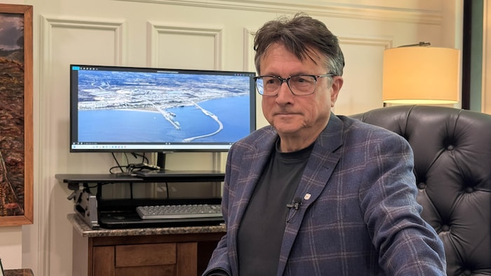 Eddy Métivier est assis à son bureau. Derrière lui, un ordinateur affiche une vue aérienne du port de Matane.