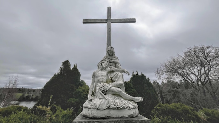 Une croix avec une statue représentant Marie et Jésus à son pied.