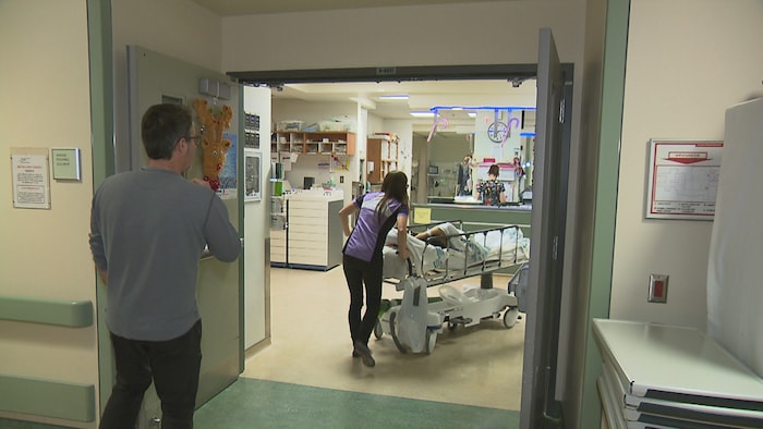 Une civière et deux employés traversent les portes de l'urgence.