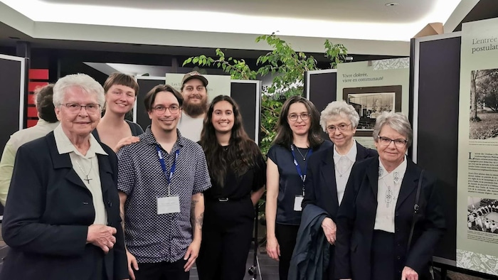 Des ursulines, des étudiants, et la professeure Karine Hébert devant des panneaux d'exposition.