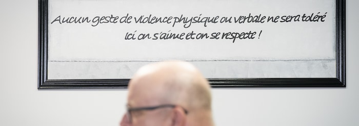 Un homme chauve devant un cadre qui dit « Aucun geste de violence physique ou verbale ne sera toléré. Ici on s'aime et on se respecte ! ».