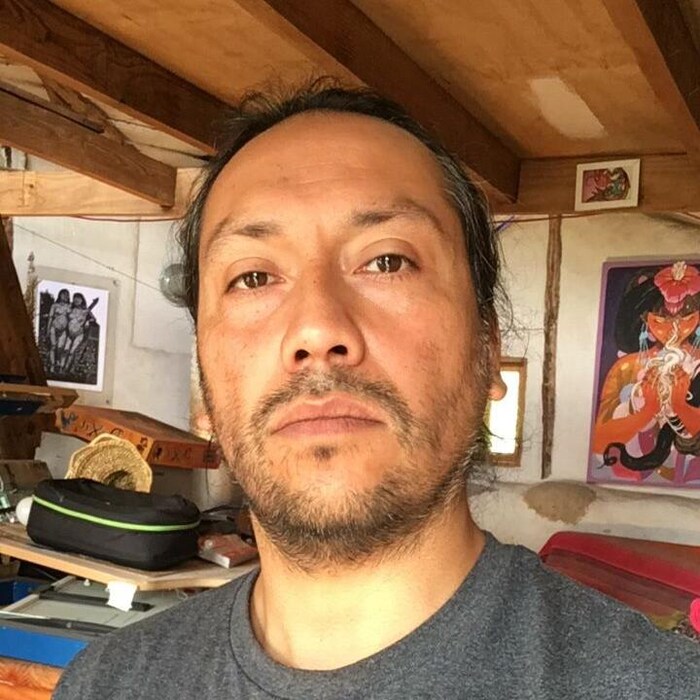 Un homme, l'artiste visuel mapuche Aner Urra, regarde la caméra d'un air sérieux.