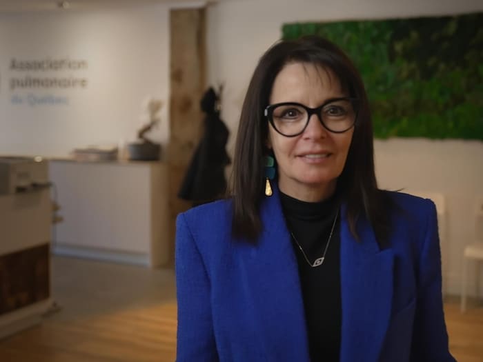 Une femme avec des lunettes et un veston bleu regarde l'objectif.