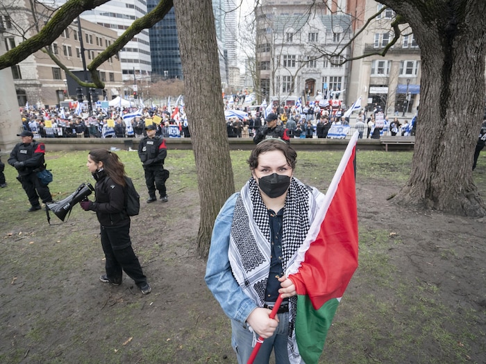 Willa Holt tient un drapeau palestinien, tandis que derrière elle, une manifestation pro-israélienne se déroule.