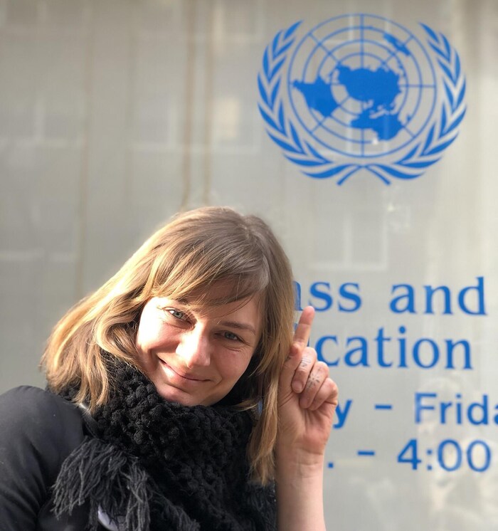 Une femme, Billie Jazz Marcuzzo-Roy, éco-éducatrice et documentariste, sourit à la caméra devant un mur à l'ONU. 
