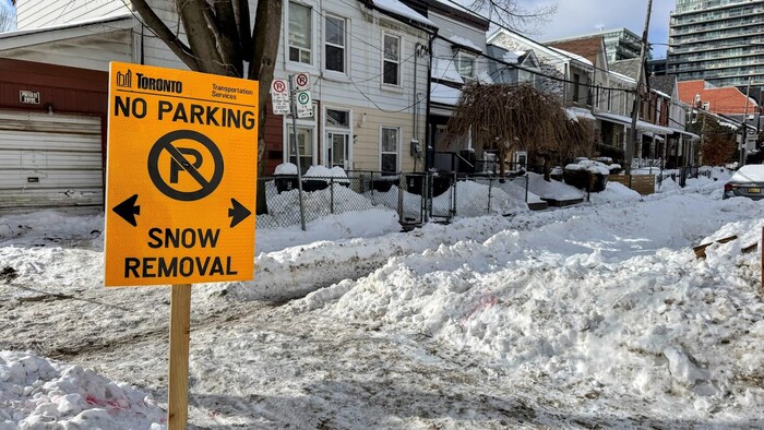 Un panneau orange temporaire indiquant que le stationnement est interdit puisqu’une opération de déneigement doit avoir lieu dans les 24 à 48 heures installé dans un amas de neige dans une rue enneigée.