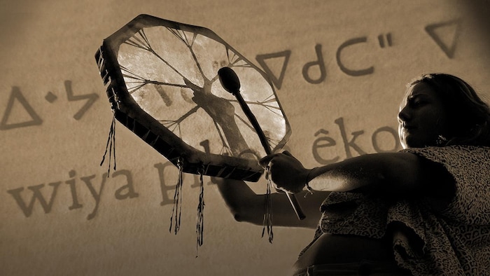 Une femme autochtone jouant du tambour; en arrière plan, du texte crie