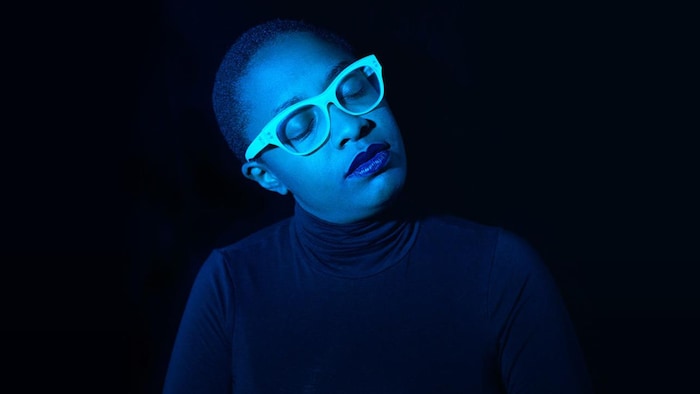 Une femme noire avec des lunettes blanches baignée dans une lumière bleue