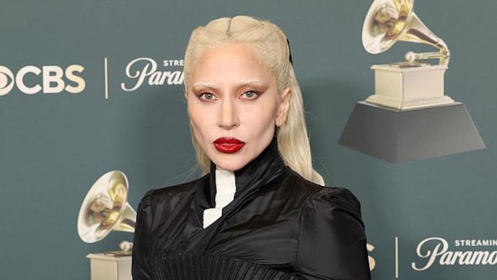 Lady Gaga pose en tenant dans ses mains deux trophées Grammy sur le tapis rouge.