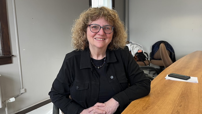 Martine Morin sourit à la caméra, assise sur une table.
