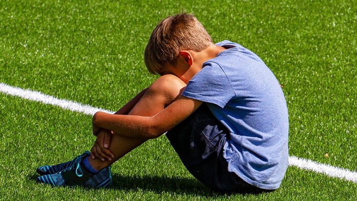 Un enfant est assis, triste, sur un terrain de sport.