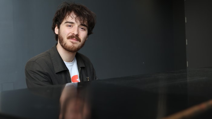 Alphonse Bisaillon est assis à un piano et il sourit.