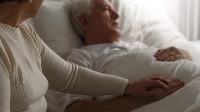 Un homme est couché dans un lit d'hôpital pendant que sa femme lui tient la main.