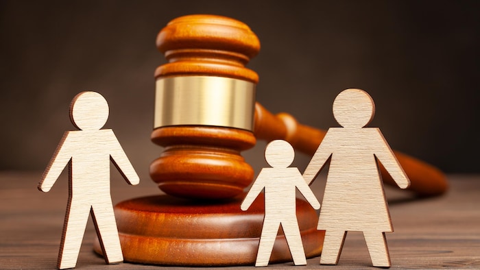 Un maillet est placé sur une table devant des petites figurines en bois d'une famille qui se sépare. L'enfant est ici confié à la mère.