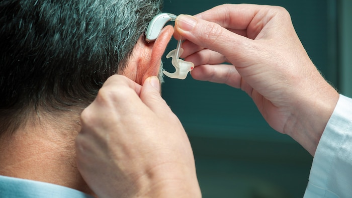 Un médecin insère un appareil auditif dans l’oreille droite d’un homme.