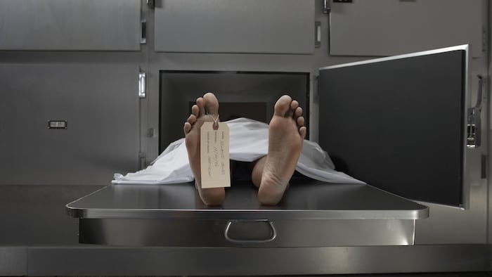 Un corps nu recouvert d'un drap blanc dans le réfrigérateur d'une salle d'autopsie. 