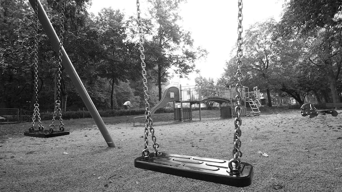 Une photo en noir et blanc d'une balançoire sur un terrain de jeux.