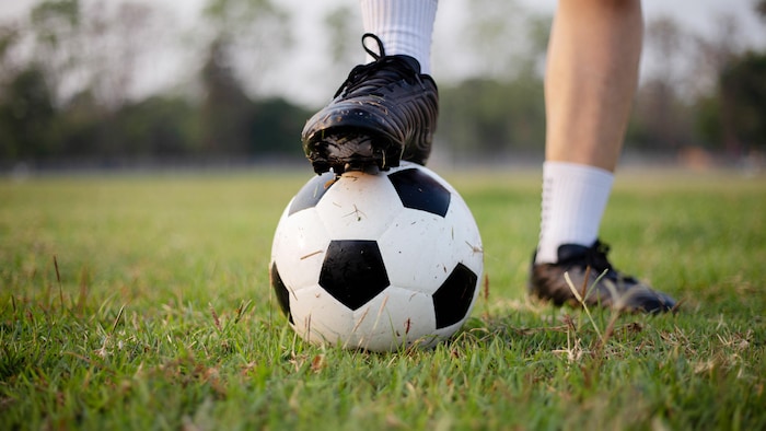 Gros plan sur le pied d'un joueur sur un ballon de soccer sur un terrain gazonné.