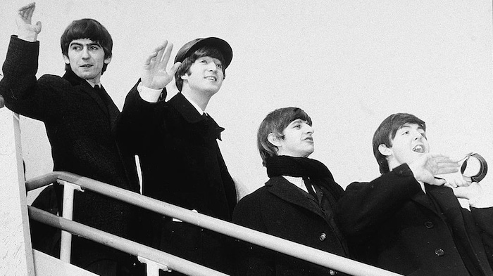 George Harrison, John Lennon, Ringo Starr et Paul McCartney sont vus sur un escalier qui les mène à bord d'un avion.