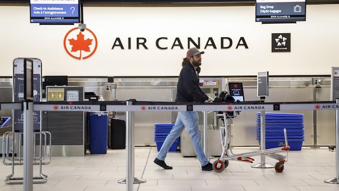 Un homme qui pousse un panier marche devant un comptoir d'enregistrement d'Air Canada dans un aéroport.