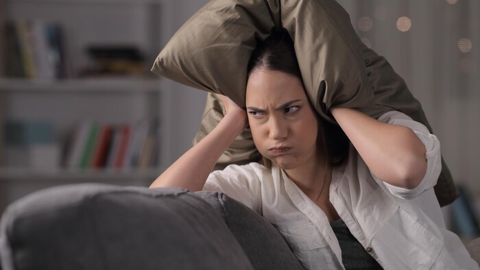 Une femme à l'allure irritée se met un oreiller sur la tête.