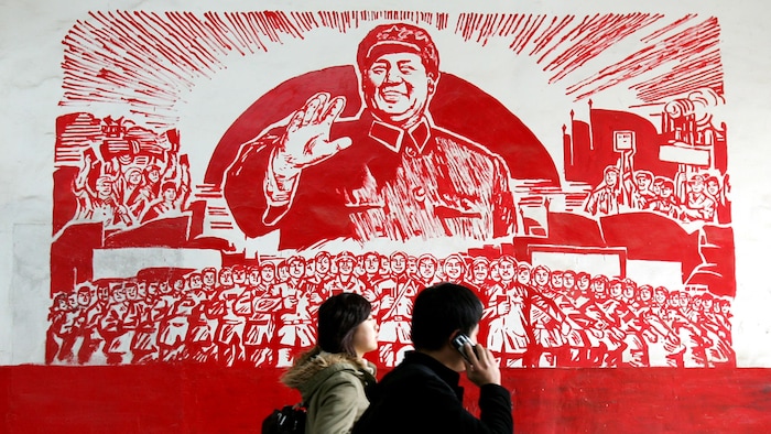 Deux personnes passent devant l'affiche qui représente le leader Mao Zedong souriant devant une foule de travailleurs.