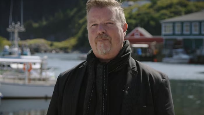 Un homme devant un paysage typique de la côte est du Canada regarde l'objectif.