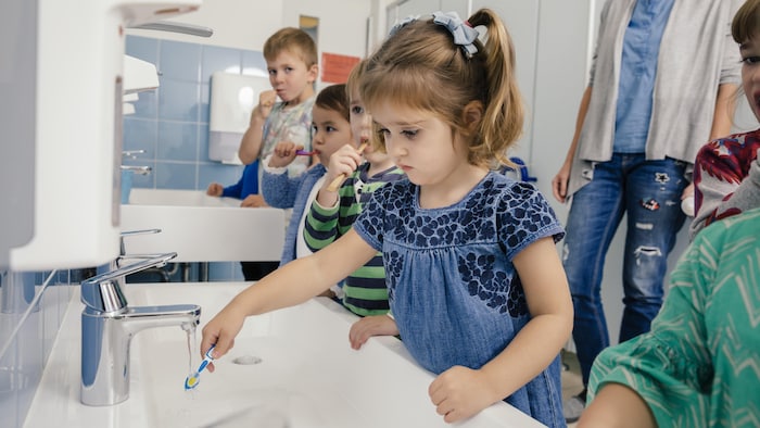 Des enfants se brossent les dents sous la supervision d'un adulte. 