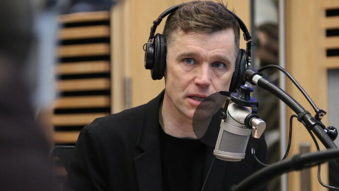 Un homme portant un casque d'écoute parle dans un micro dans un studio de radio. 