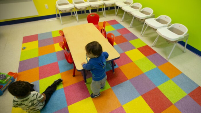 Deux enfants dans une salle aux murs et au sol colorés et avec des chaises pour enfants. 