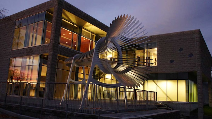 Vue extérieure du Centre des arts de Baie-Comeau à la tombée du jour avec une grande sculpture métallique devant l'entrée.