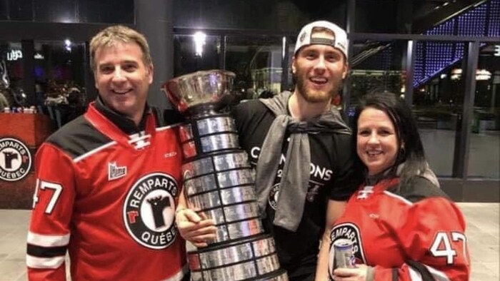 Le hockeyeur Charle Truchon tenant la coupe Memorial dans ses bras avec son père et sa mère.