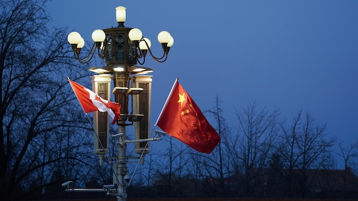 Le soir, un drapeau du Canada et un drapeau de la Chine flottent côte à côte sur un lampadaire allumé.