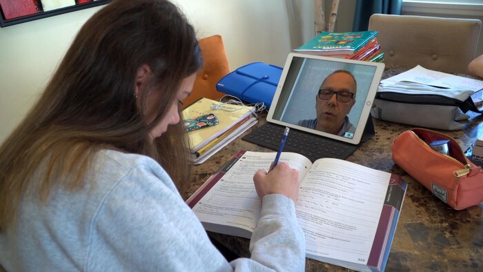 Une élève écoute son enseignant sur une tablette électronique pendant qu'elle réalise des exercices.