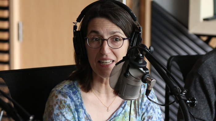 Une femme parle dans un micro, dans un studio de radio. 