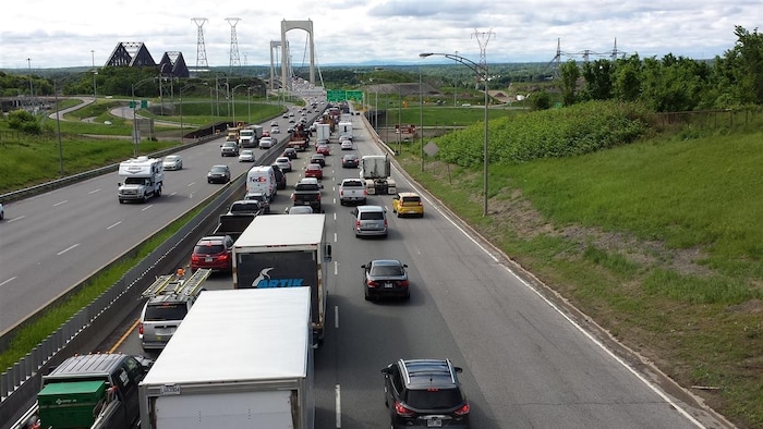 Des voitures circulent au ralenti sur l’autoroute Henri-IV, en direction sud, à l’approche du pont Pierre-Laporte, qu’on aperçoit au loin. Le pont de Québec est également visible. La photo a été prise de jour, en été.