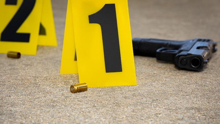 Une scène de crime sur laquelle se trouvent un pistolet et deux douilles par terre.