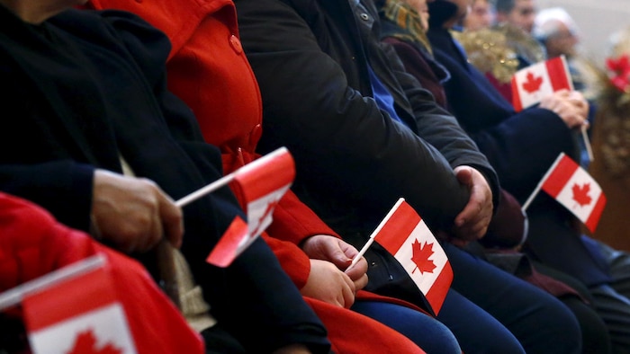Des personnes assises tiennent des drapeaux canadiens dans leurs mains.