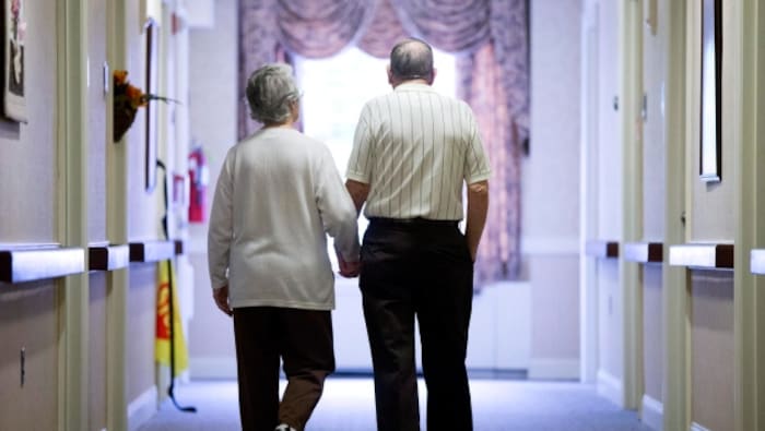 Un couple de personnes âgées marche dans un couloir d'hôpital en se tenant la main.